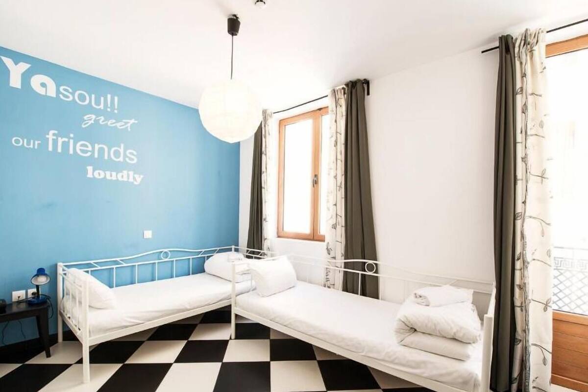 Una habitación con dos literas, una pared azul con una cita motivacional, una ventana con cortinas y un suelo a cuadros.