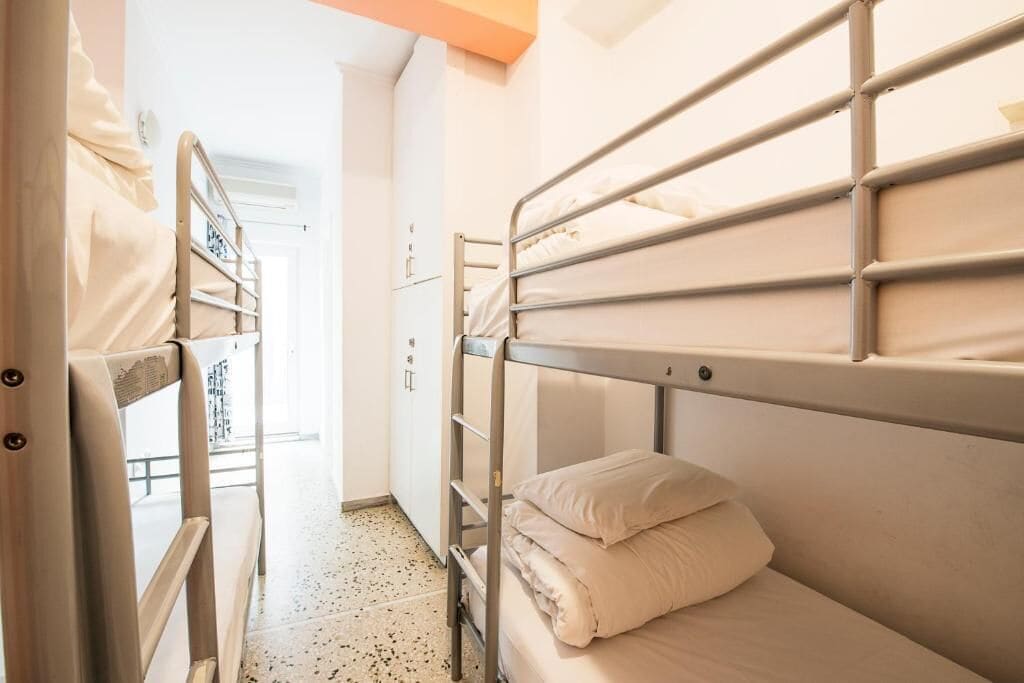 Une chambre de dortoir avec des lits superposés, une armoire et une porte donnant sur une autre pièce.