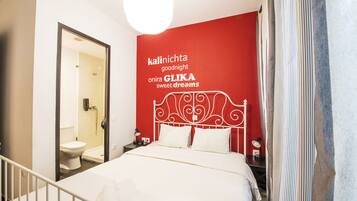 A hotel room with a red accent wall, a white bed, and a bathroom visible through an open door.