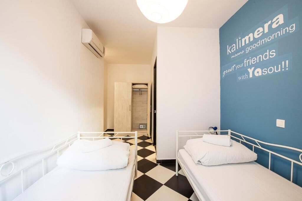 A room with two single beds, a black and white checkered floor, a blue accent wall with text, and a white ceiling light.