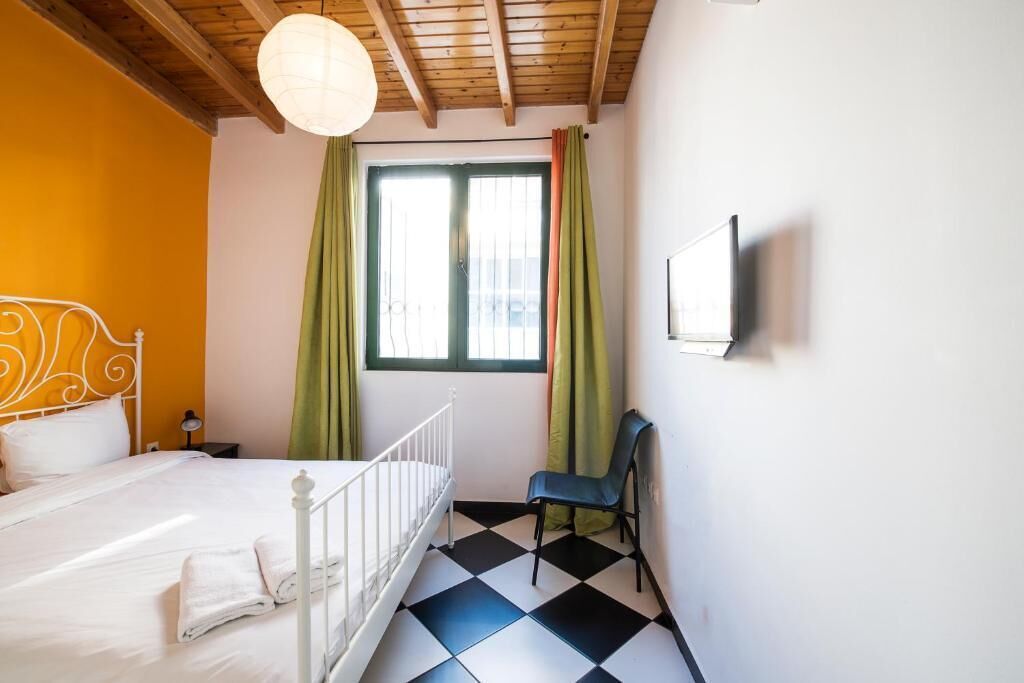 Een kamer met een bed, een stoel, een raam met gordijnen en een tv aan de muur.
