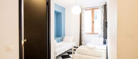 Una habitació amb dos llits, un sòl de quadres, una paret d'accent blava i una finestra amb cortines.