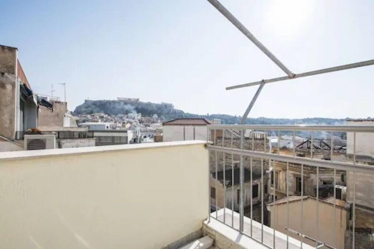 Terraza en la azotea con barandilla metálica, con vistas a un paisaje urbano que incluye edificios y una colina distante.