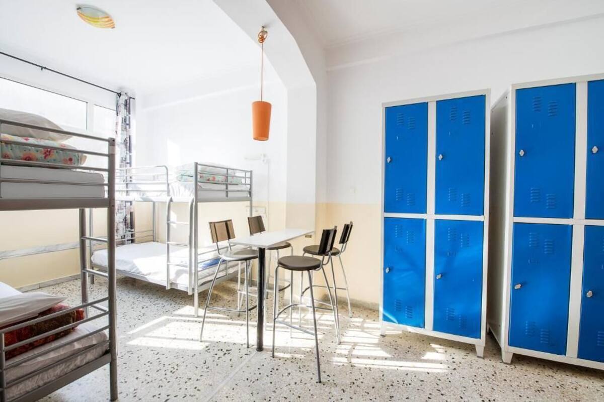 Un dormitorio con literas, una mesa, sillas y taquillas azules.