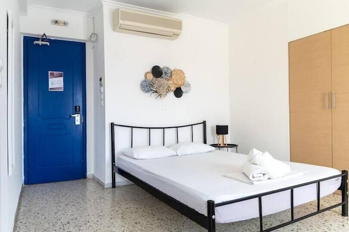 Un dormitorio con cama, una puerta azul, un armario y un aire acondicionado instalado en la pared.