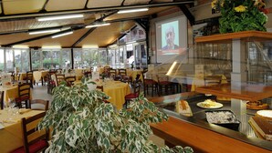 A restaurant with tables and chairs, a projection screen, and a display case with desserts. - Hotel Puntabella (Varazze)