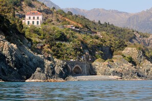A coastal house with a stone bridge leading to a rocky beach.