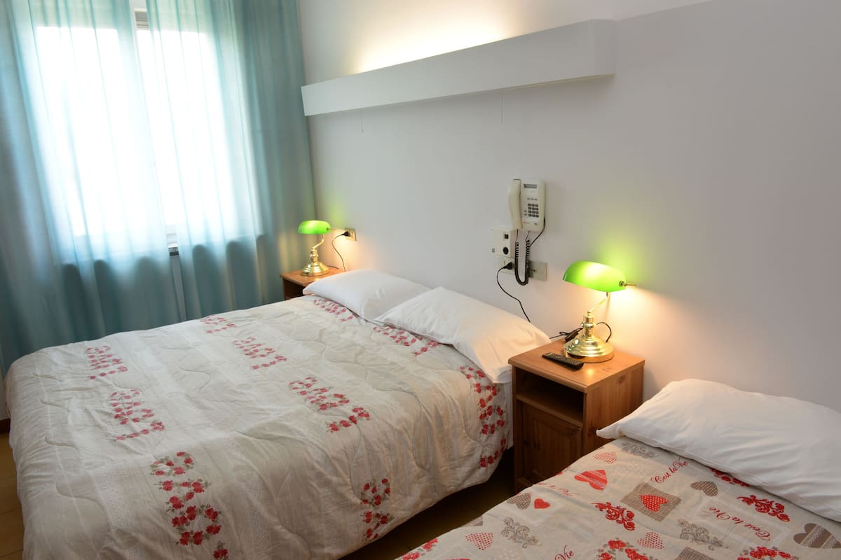 A bedroom with a bed, two bedside lamps, a telephone, and a window with curtains.