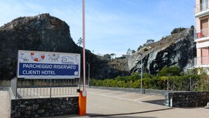 A sign for Parcheggio Riservato Clienti Hotel with a view of rocky terrain and a building in the background. - Hotel Puntabella (Varazze)