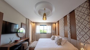 Habitación de hotel moderna con una cama grande, un televisor de pantalla plana, un escritorio con espejo y una ventana con cortinas.