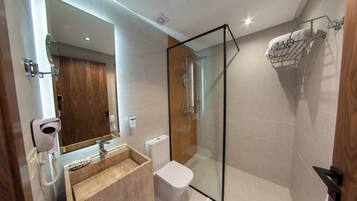 A modern bathroom with a glass-enclosed shower, a wooden vanity, a toilet, and a towel rack.