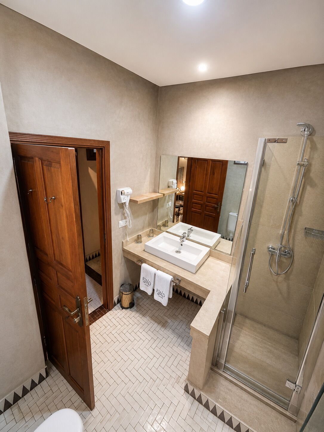 A bathroom with a wooden door, a shower, a sink with a mirror, and a towel rack.