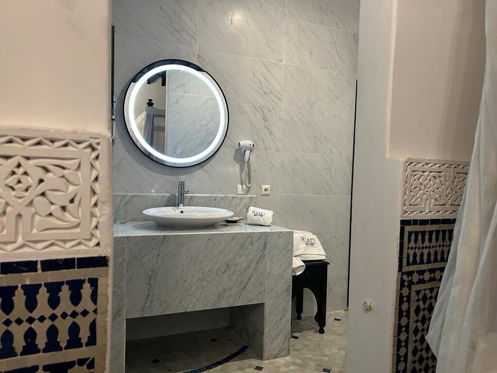 A bathroom with a marble sink, a round mirror, and a hairdryer.