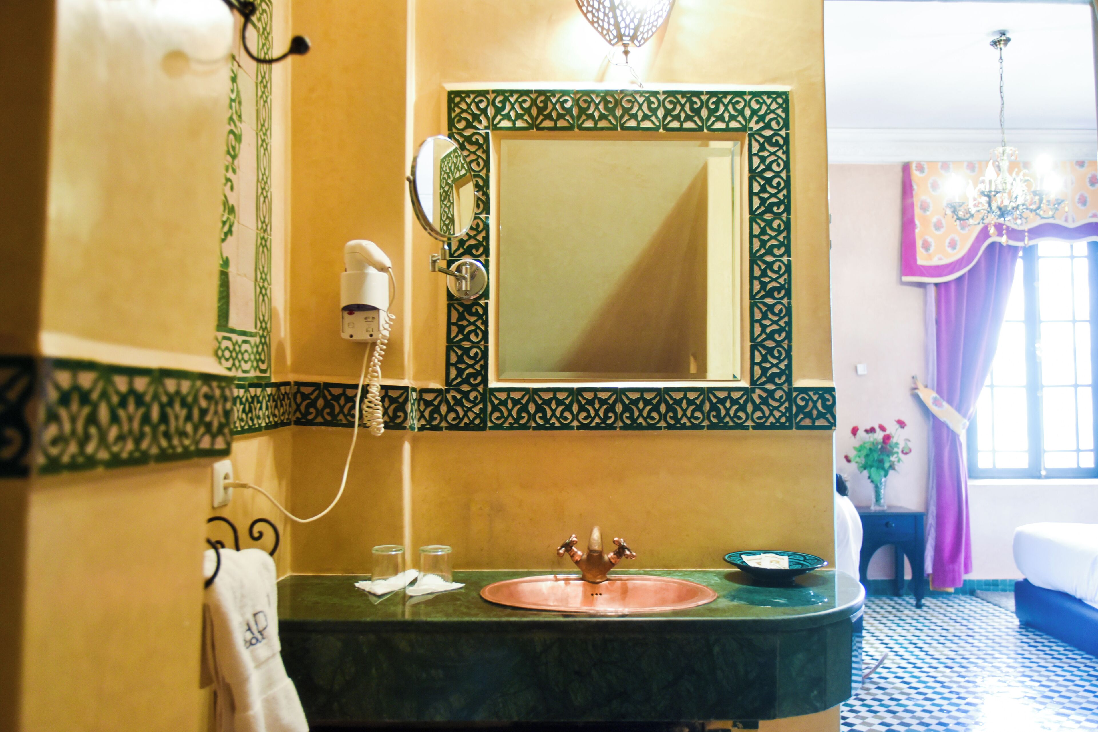 A bathroom with a green-tiled sink, a mirror, a hairdryer, and a window with curtains.