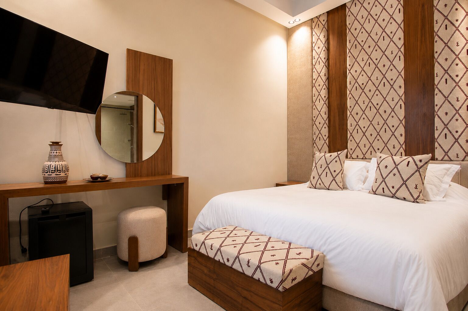 A hotel room with a bed, bedside table, mirror, and a TV mounted on the wall.