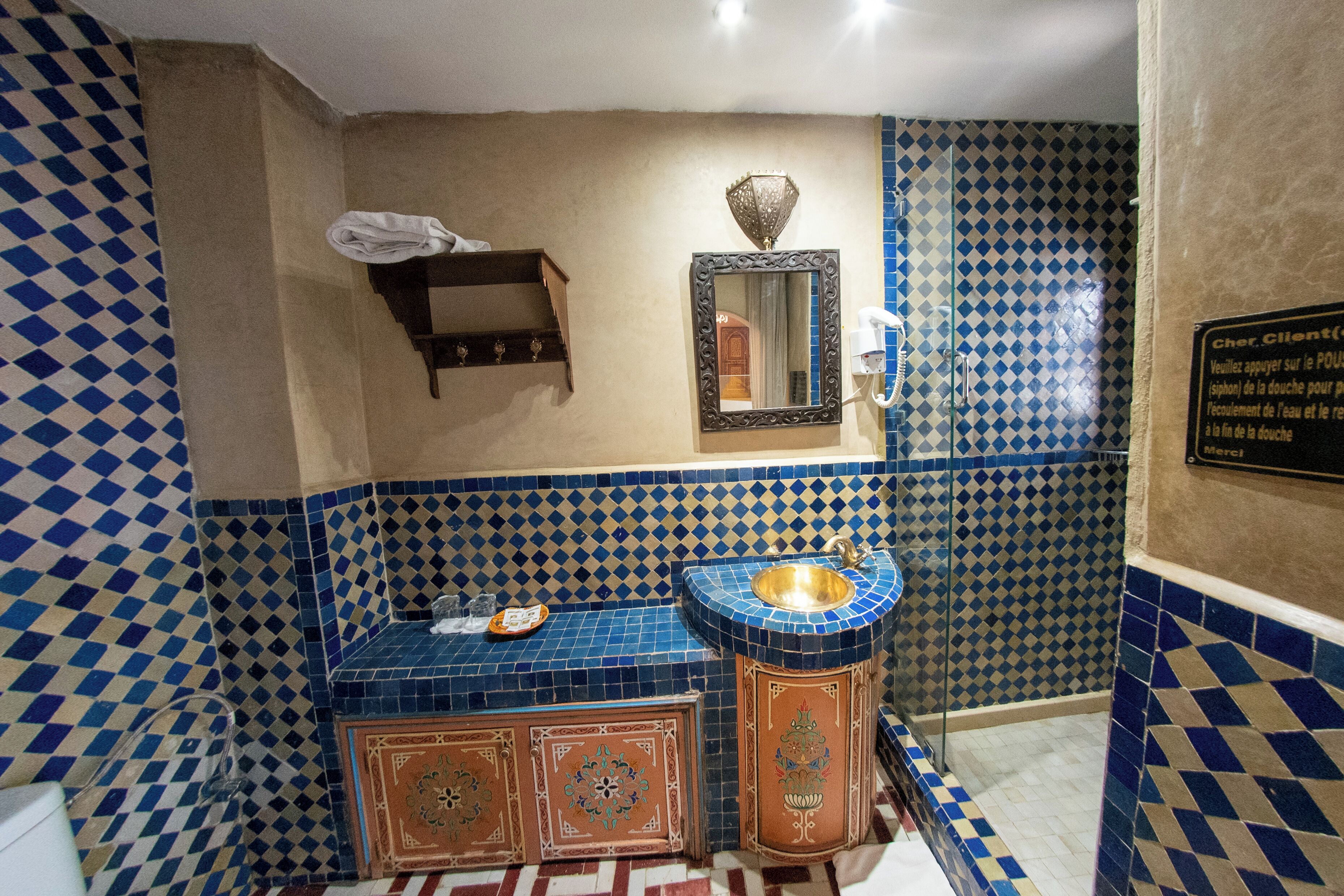 Een badkamer met een blauw-beige geruite vloertegel, een wastafel met een gouden kom en een spiegel erboven.