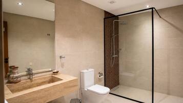 A modern bathroom with a glass-enclosed shower, a beige-tiled sink, and a white toilet.