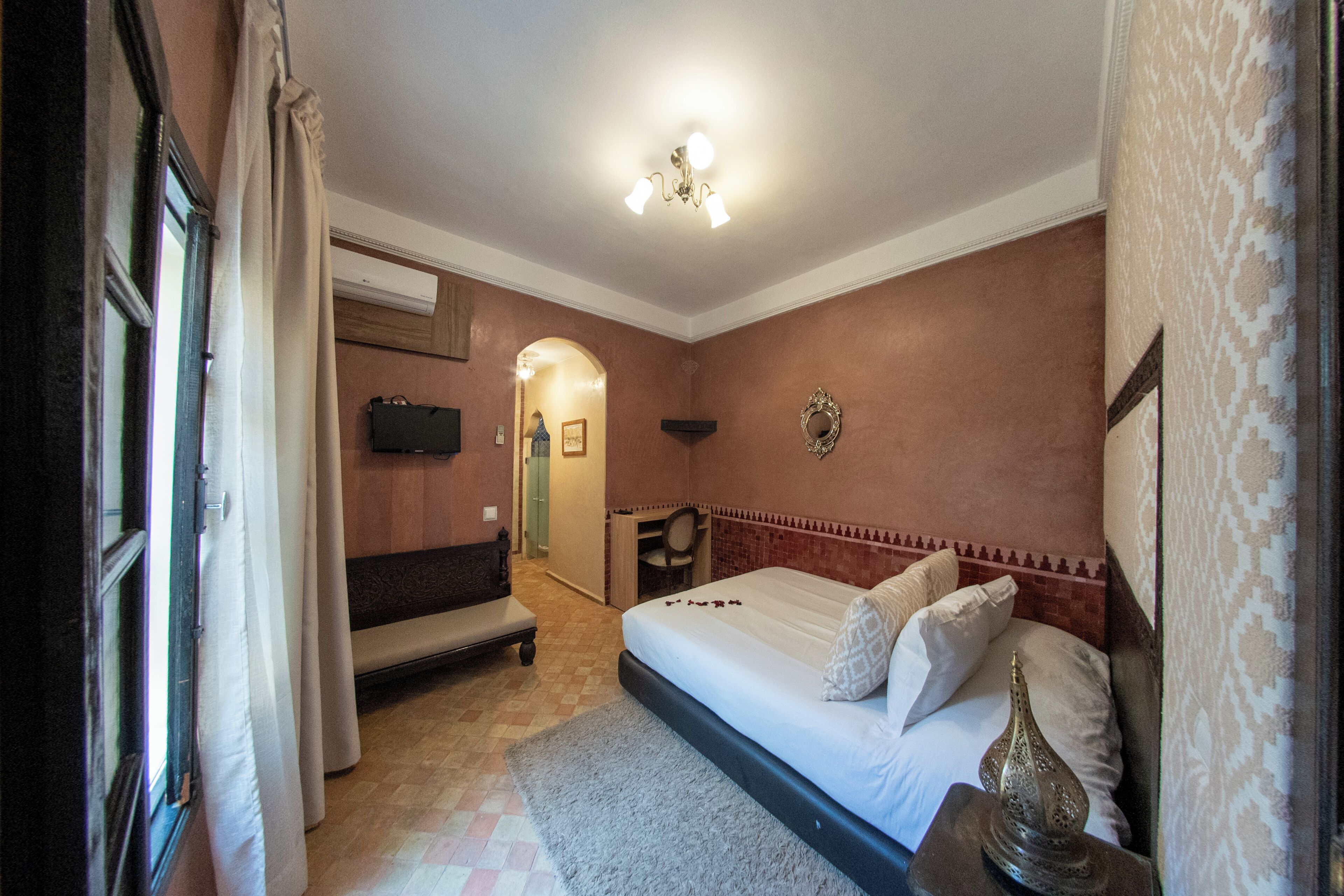 Una habitación de hotel con cama, un banco, un escritorio, un espejo y televisión.