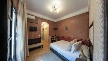 Una habitación de hotel con cama, un banco, un escritorio, un espejo y televisión.