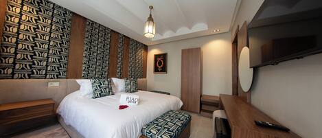 Une chambre moderne avec un lit, des tables de chevet, un banc, un téléviseur et un mur décoré d’un motif.