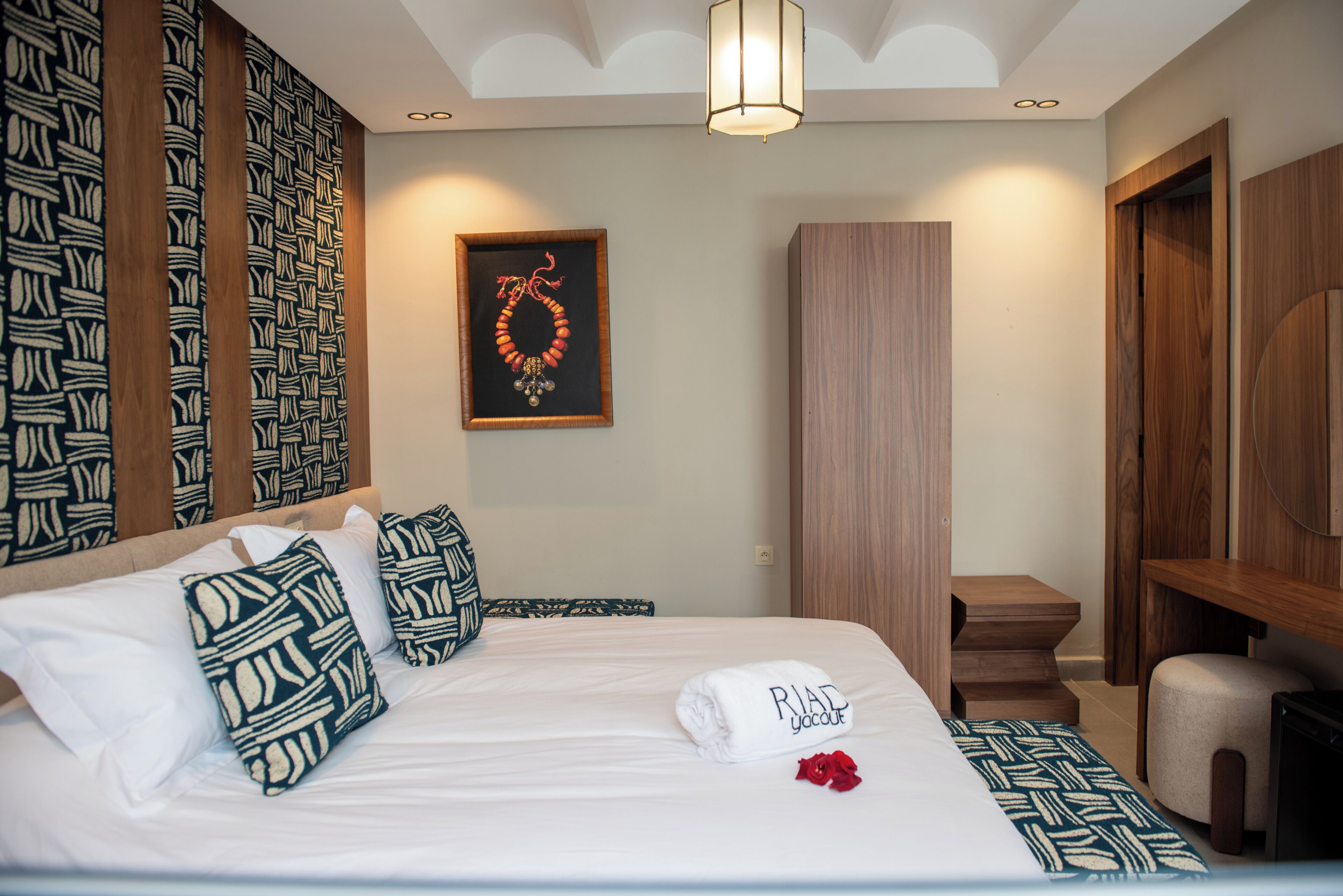 Une chambre d’hôtel comprenant un lit, des oreillers, un tableau encadré, une armoire en bois et un petit coin salon.