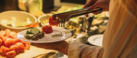 A buffet with various food items including tomatoes, cucumbers, and olives.