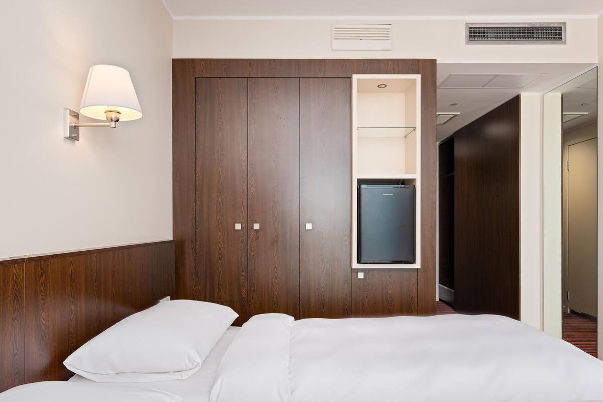 Ein Hotelzimmer mit einem Bett, einem an der Wand befestigten Fernseher und einem Schrank mit Spiegel.