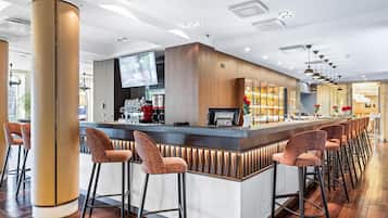 A modern bar area with a long counter, multiple stools, and a television screen.