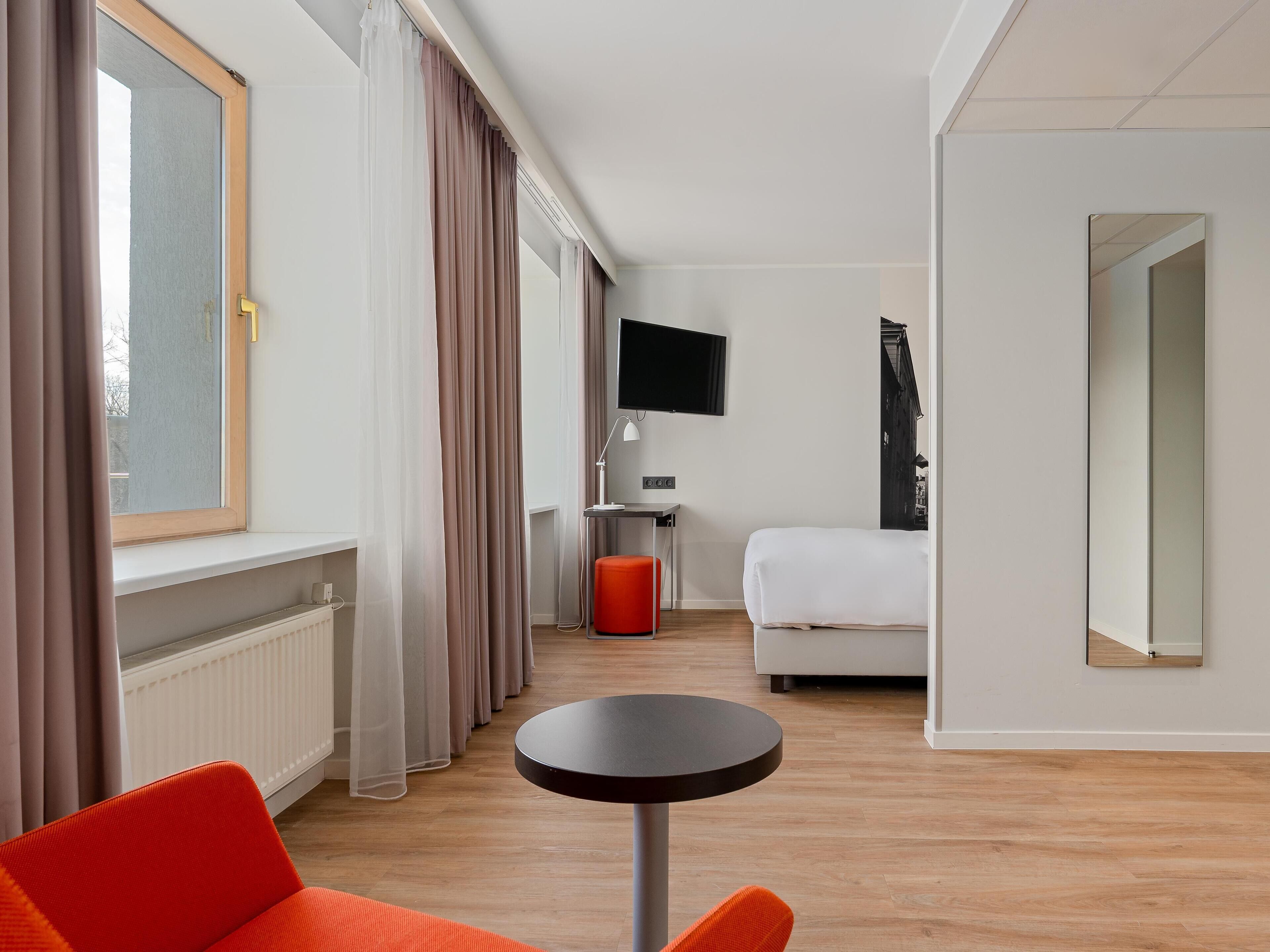 Ett hotellrum med en säng, ett skrivbord med en dator, en tv och ett runt bord.
