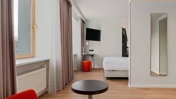 Ett hotellrum med en säng, ett skrivbord med en dator, en tv och ett runt bord.