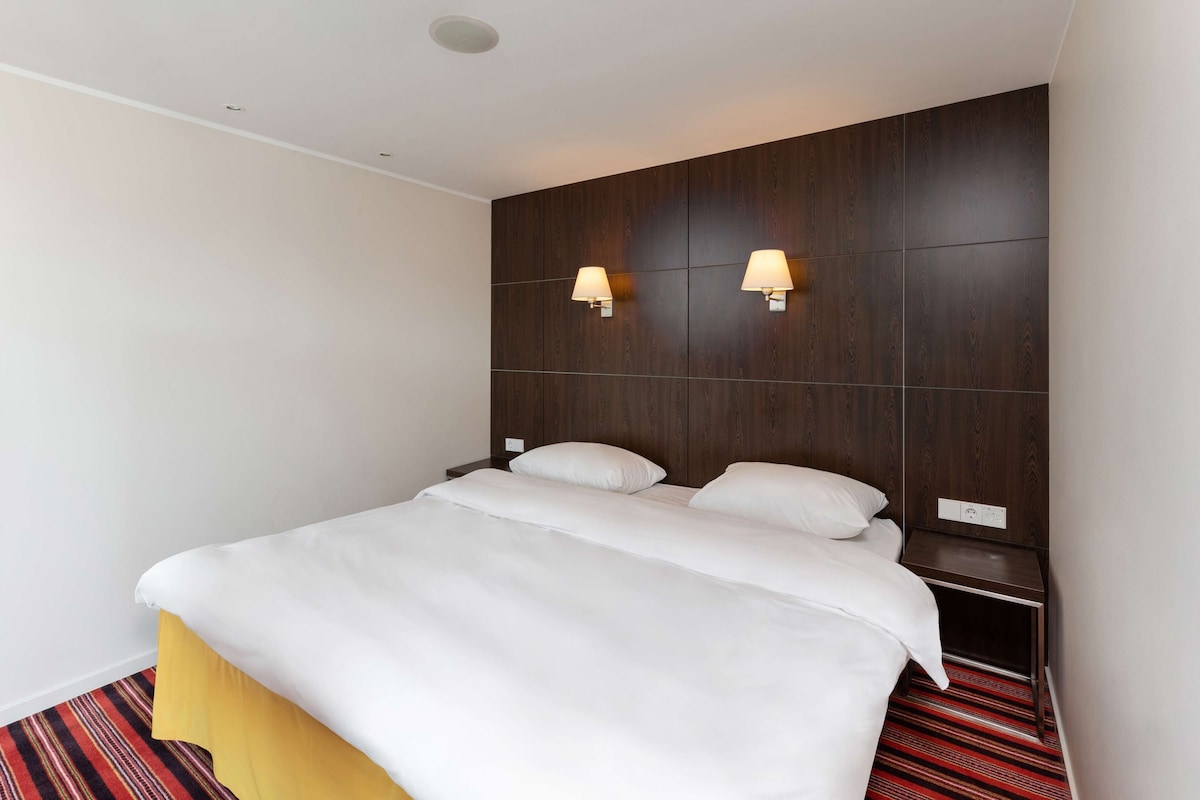 A hotel room with a bed, two bedside tables, and wall-mounted lamps.