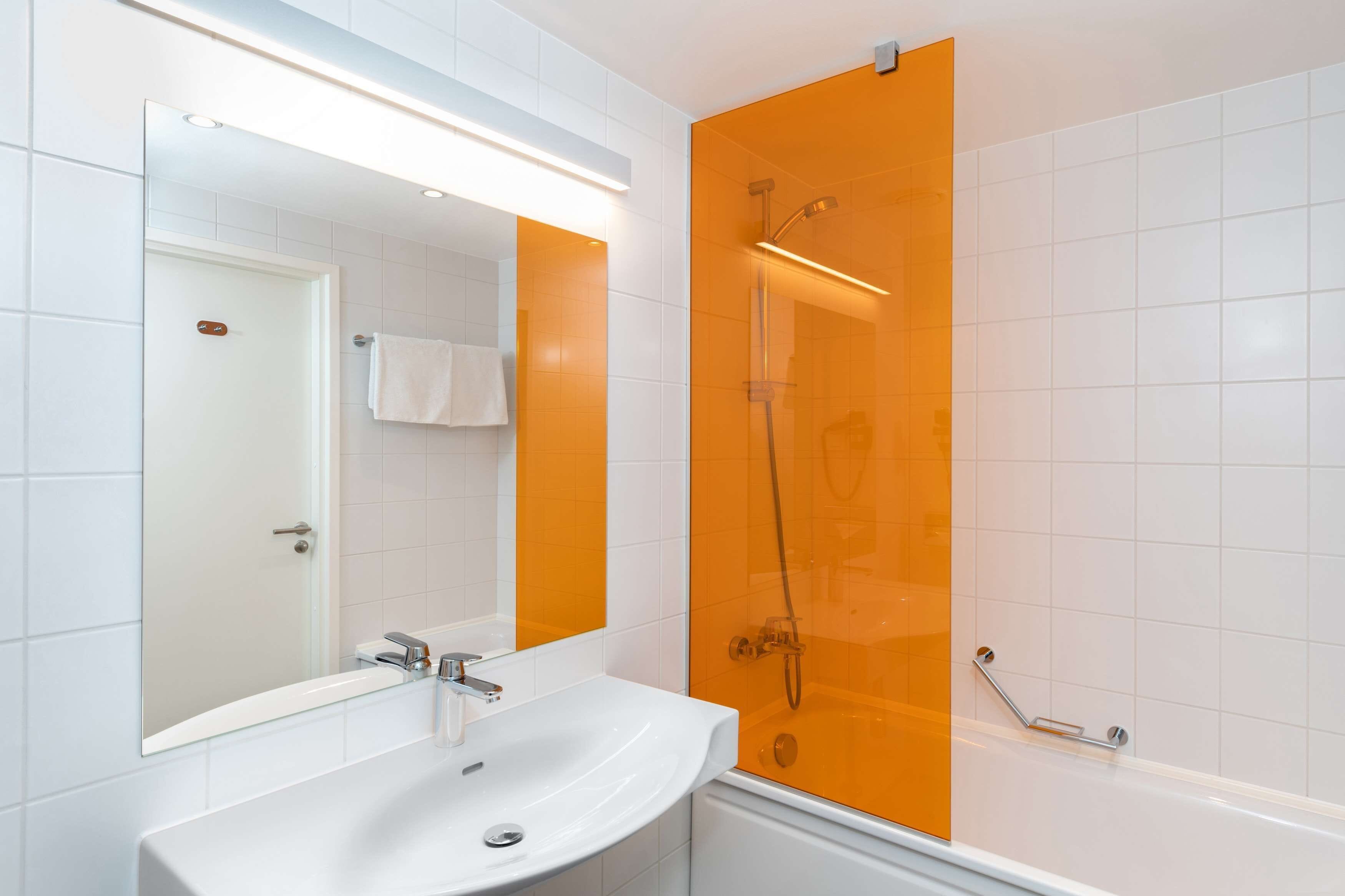 A bathroom with a white sink, a mirror, and an orange shower enclosure.