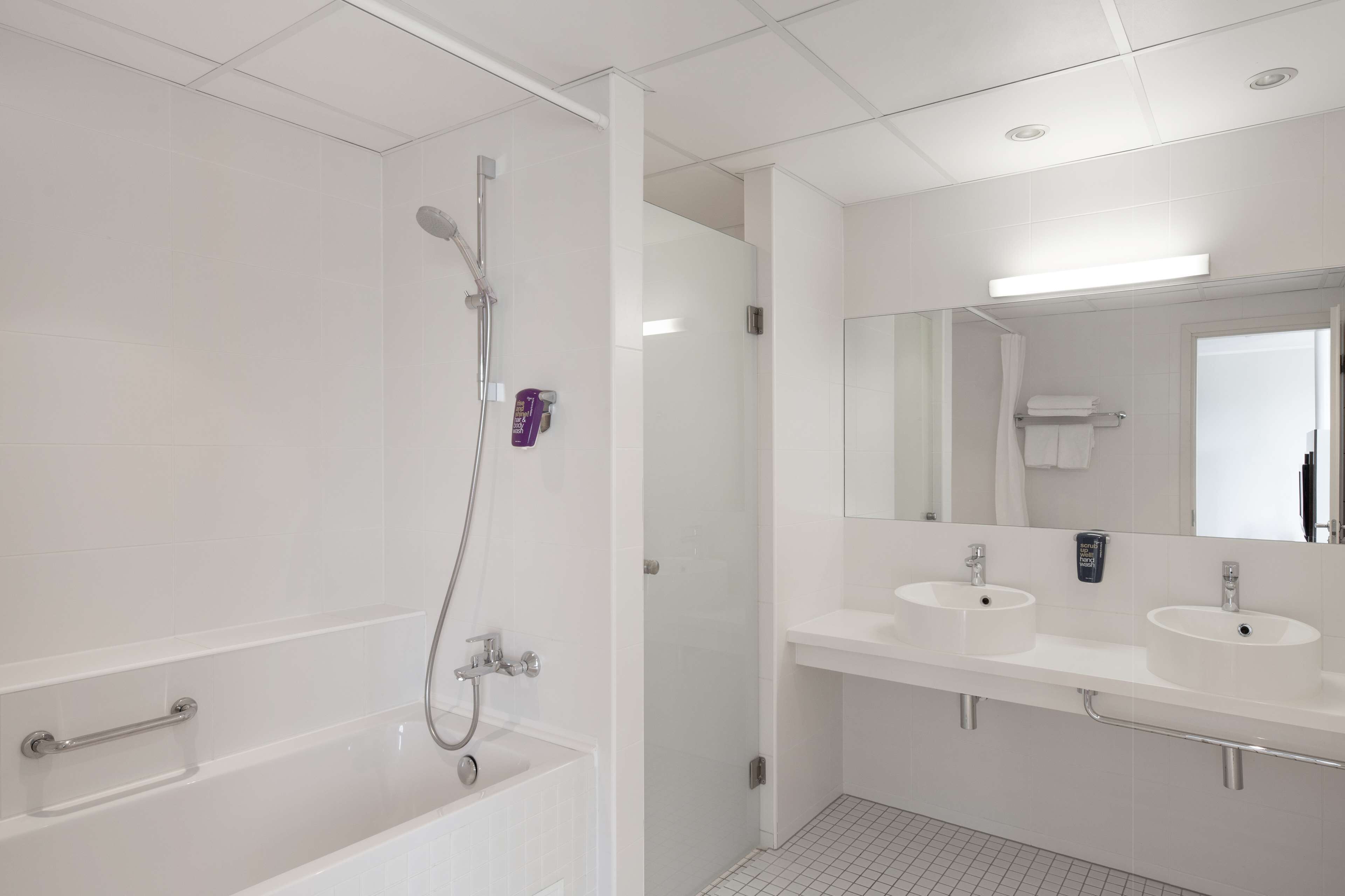 A modern bathroom with a bathtub, two sinks, a shower, and a large mirror.
