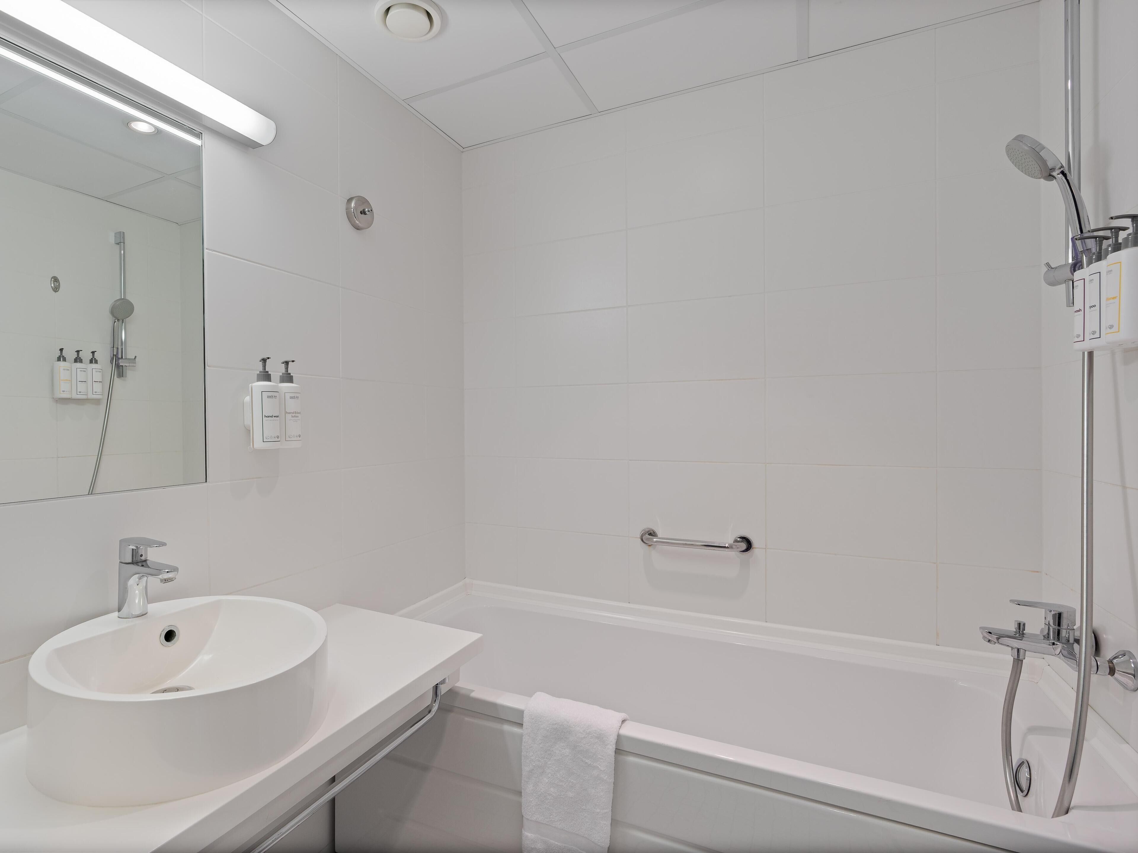 A modern bathroom with a white sink, mirror, and bathtub.