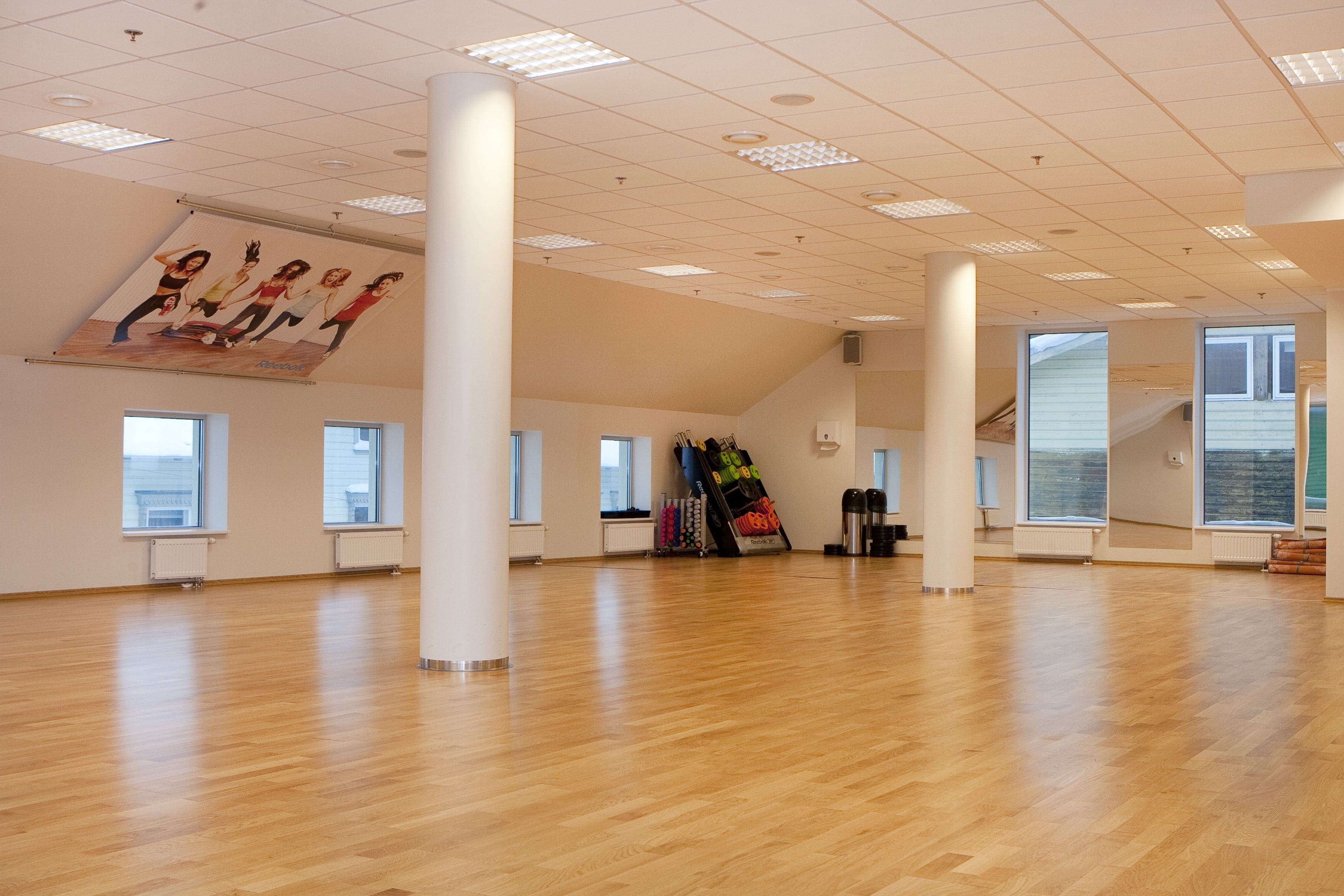 A spacious room with wooden flooring, large windows, and a ceiling with recessed lighting.
