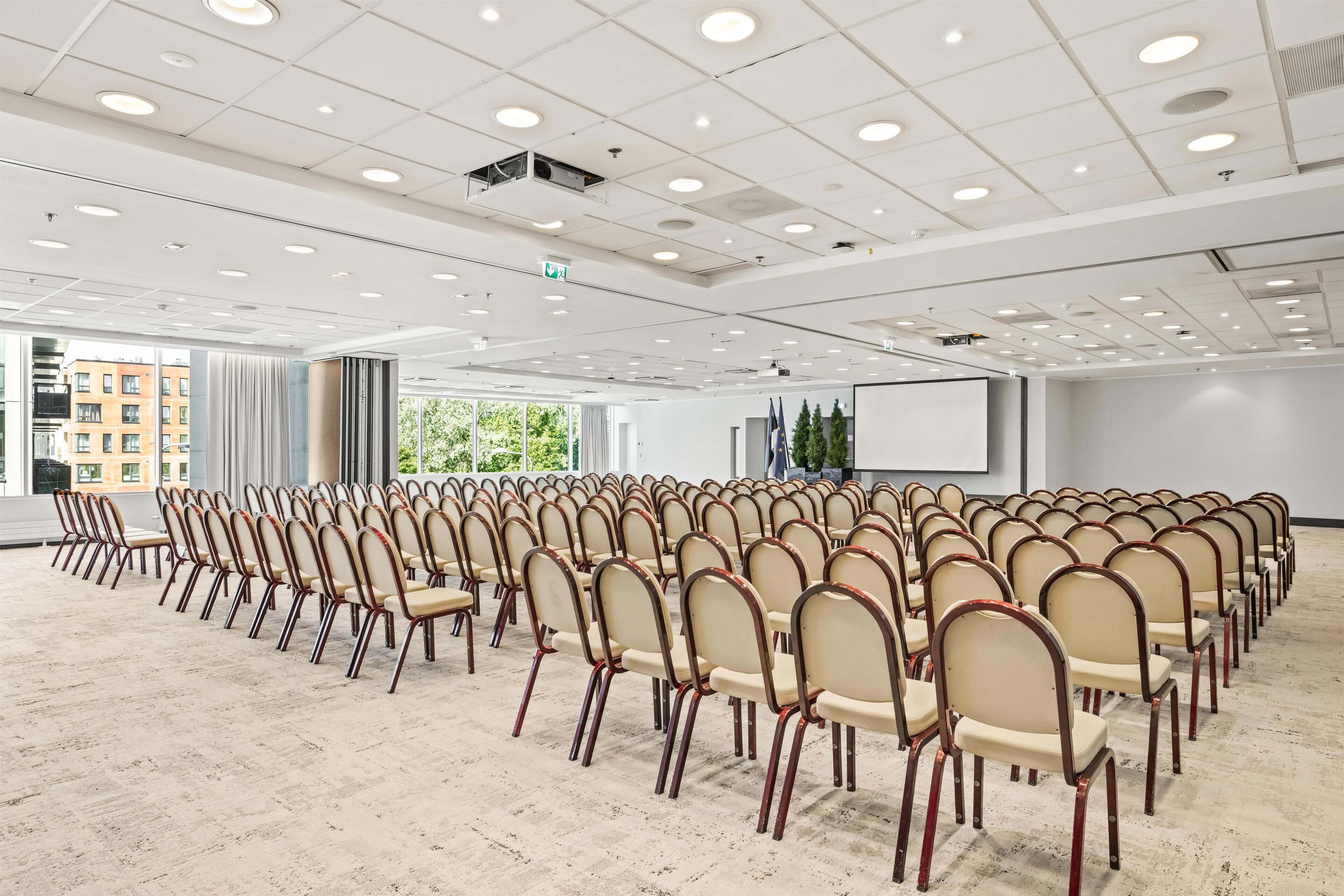 A conference room with rows of chairs, a projector screen, and large windows.
