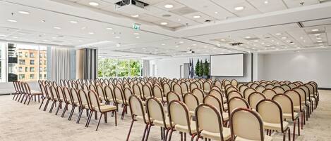 A conference room with rows of chairs, a projector screen, and large windows.