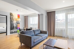 A modern hotel room with a grey sofa, wooden flooring, a dining table, and large windows with curtains. - Park Inn by Radisson Meriton Conference & Spa Hotel Tallinn (Tallinn)