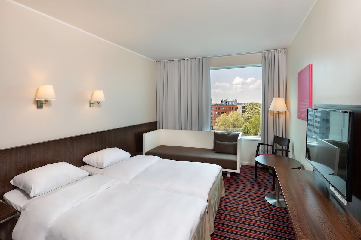 A hotel room with a large bed, a sofa, a TV, and a window with curtains.