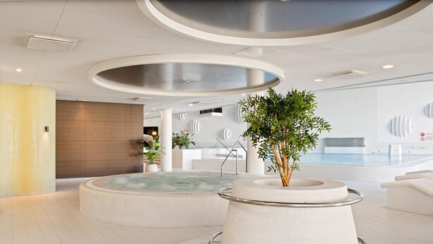 A modern indoor pool area with a central hot tub, surrounded by seating and a staircase leading to a lower level. - Park Inn by Radisson Meriton Conference & Spa Hotel Tallinn (Tallinn)