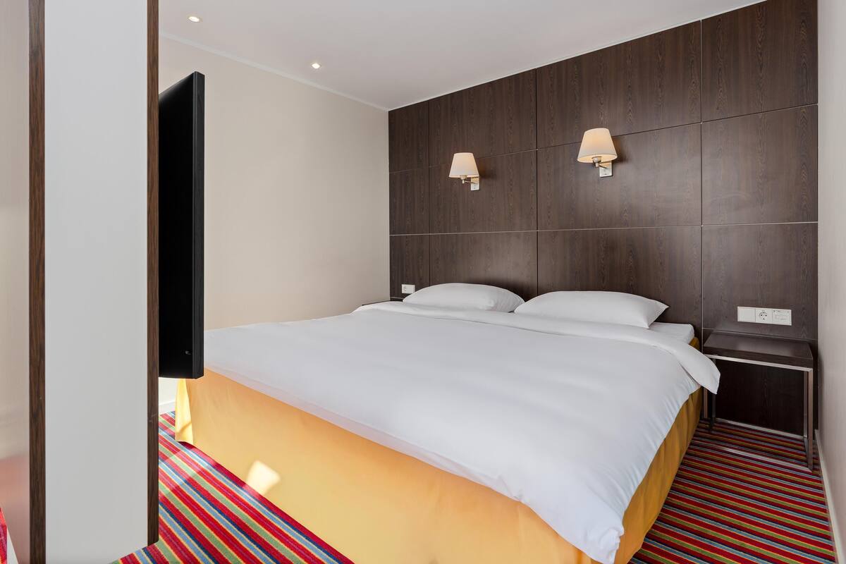 Ein Hotelzimmer mit einem Bett, zwei Wandlampen, einer Steckdose und einem Streifen Teppich.