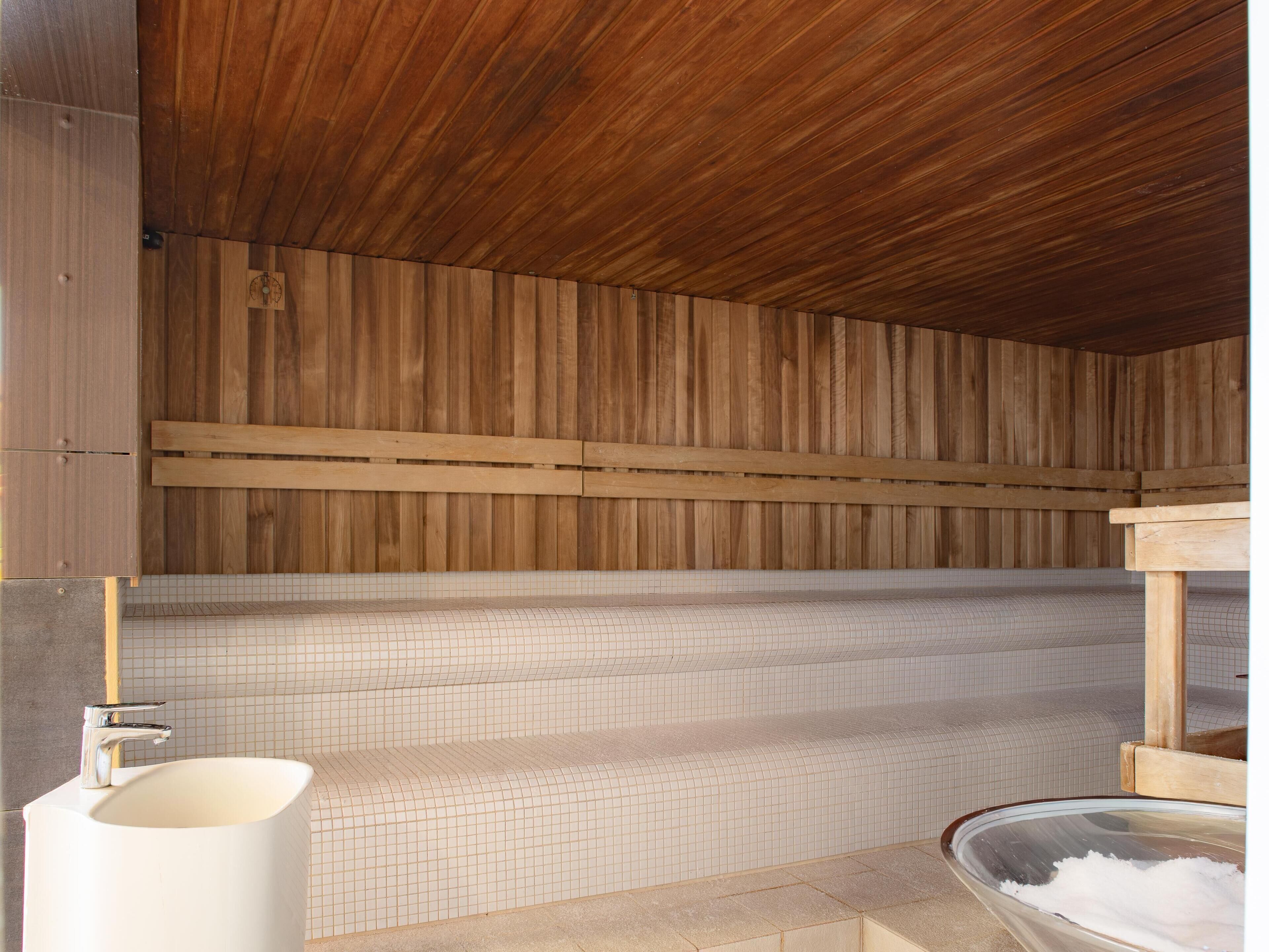 A wooden sauna with a tiled floor, a white sink, and a wooden bench.