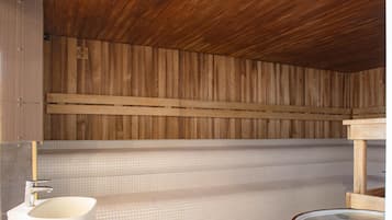 Una sauna de madera con suelo de baldosas, un lavamanos blanco y un banco de madera.