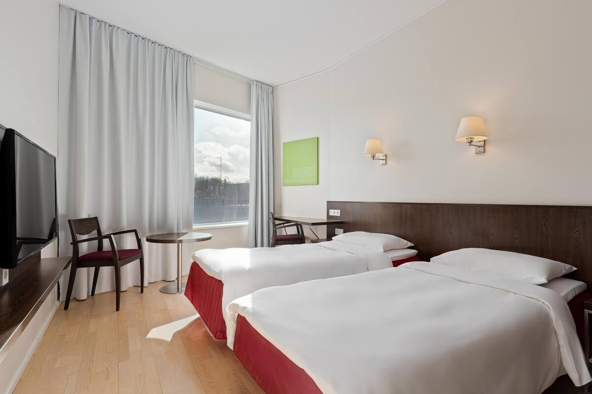 Ein Hotelzimmer mit zwei Betten, einem Fernseher, einem Schreibtisch und einem Sessel.