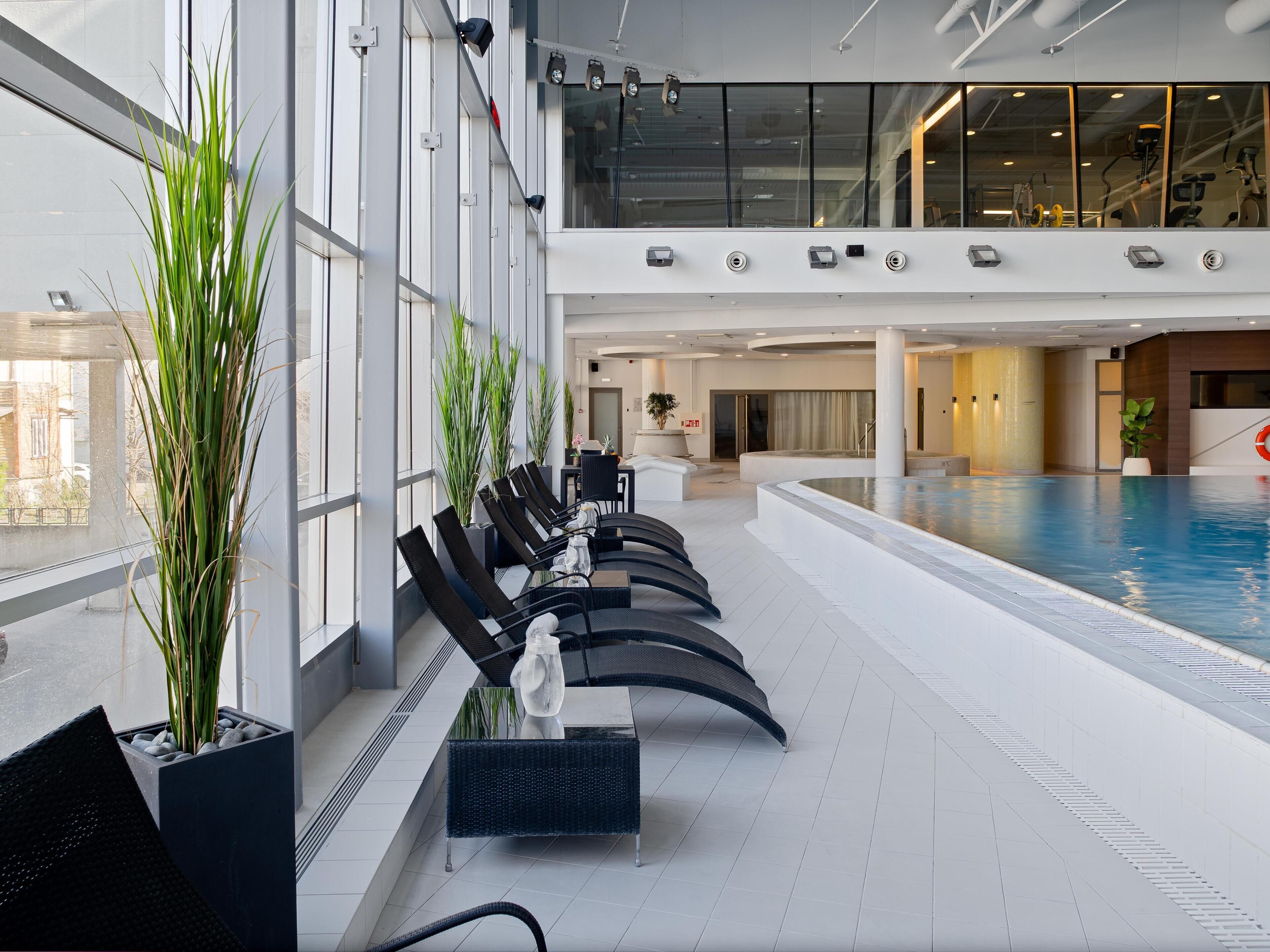 Una piscina interior con asientos, ventanas amplias y plantas de interior.