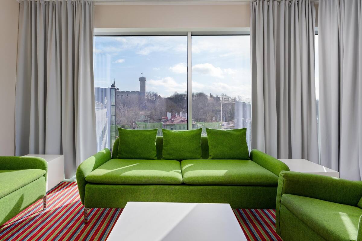 Ein modernes Hotelzimmer mit großem Fenster, einem grünen Sofa und einem Streifenmuster-Teppich.