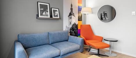 Una sala de estar moderna con un sofá azul, un sillón naranja, un espejo redondo y una pequeña mesa circular.