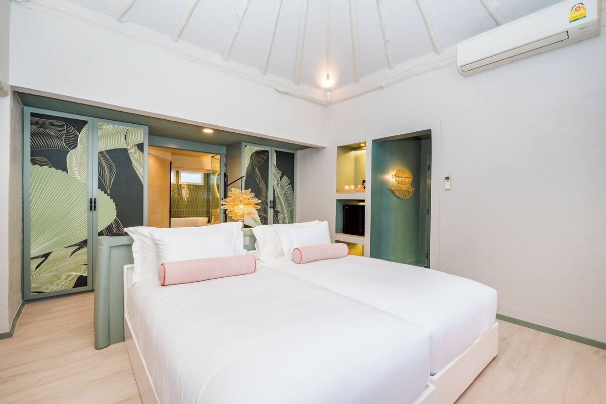 Une chambre d’hôtel avec un grand lit, une armoire, un miroir et un petit coin salon avec une lampe.