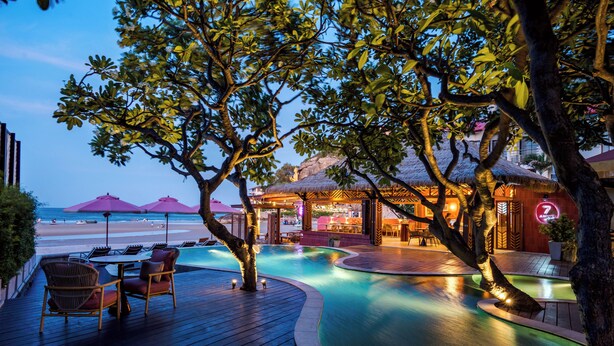 Un espace aménagé au bord de la piscine, avec une structure à toit de chaume, une terrasse en bois et des chaises longues.