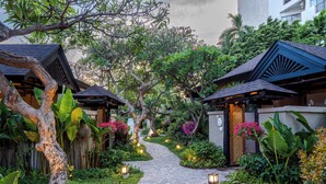 Un chemin menant à un bâtiment à l’architecture traditionnelle, entouré d’une végétation luxuriante et de plantes en fleurs.
